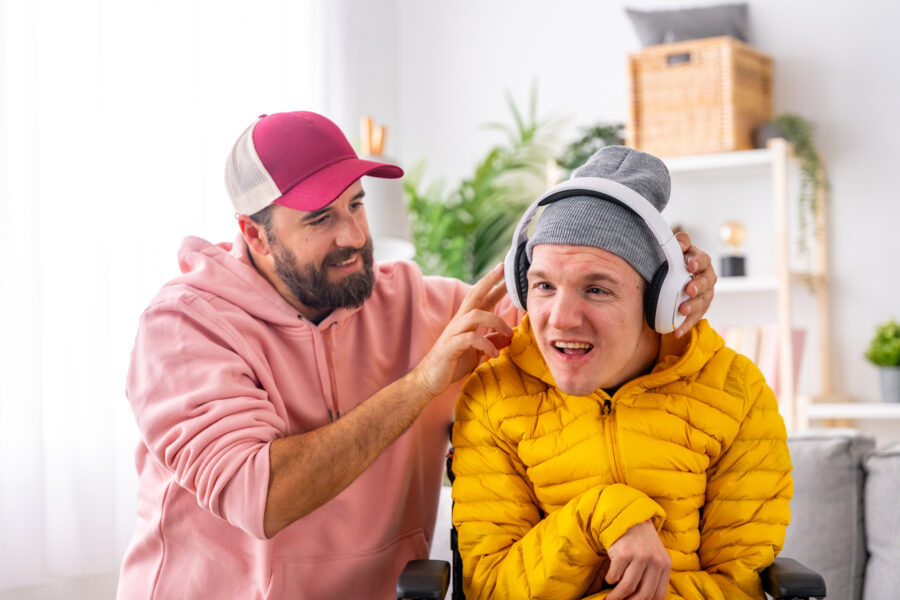 Disabled man using headphones listening to music with carer is a NDIS_MTA_guest_with_medistays_wheelchair_accessible_medium_term_accommodation_in_australia