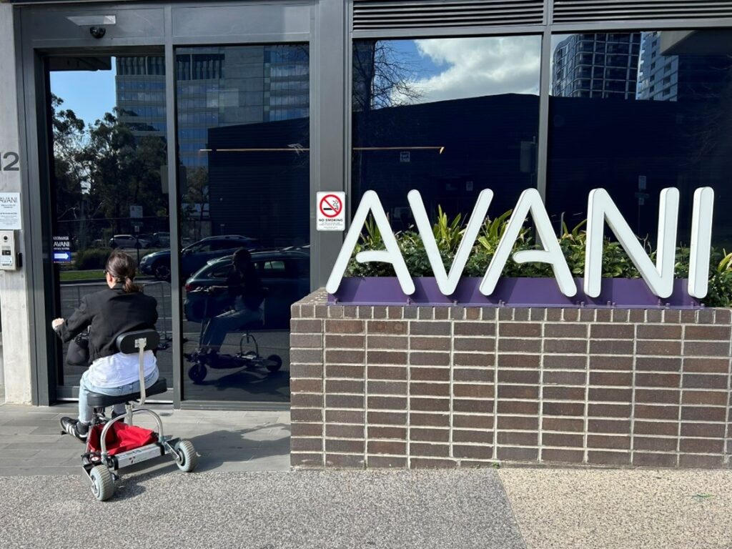 lady on mobility scooter entering the front of a hotel called AVANI