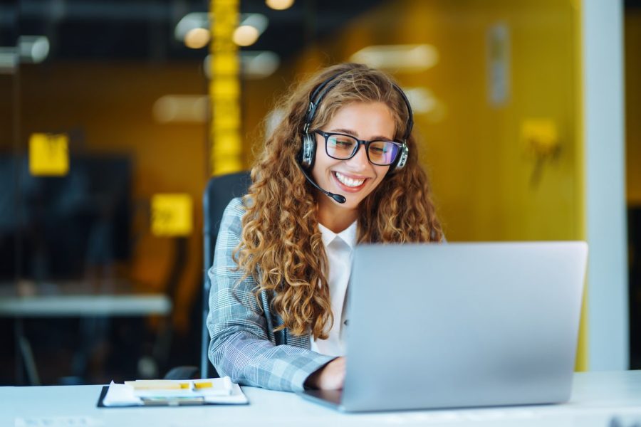 A MediStays Care Navigator is wearing a headset and smiling as she looks down at her laptop to book a guests medical accommodation.