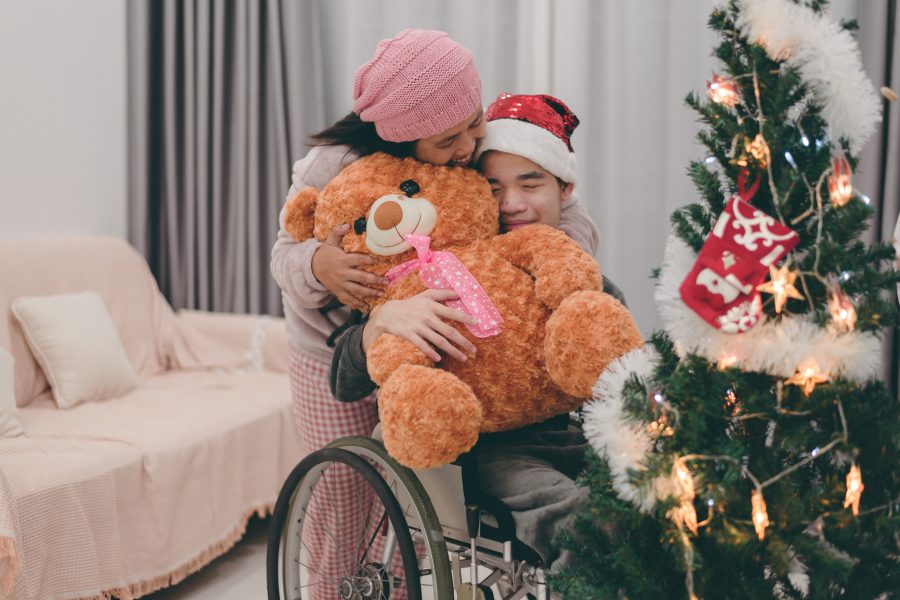 Big brown teddy bear from mother to teenage boy with disability on wheelchair and christmas tree,Gift making smile and joy,Festival of happiness and giving Merry Christmas and Happy New Year concept.