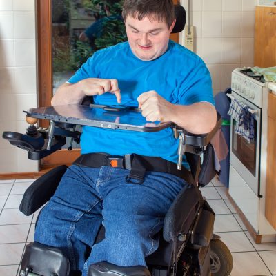 Spastic young man confined to a multifunctional wheelchair as a result of infantile cerebral palsy caused by birth complications, dialing a number on his smart phone.